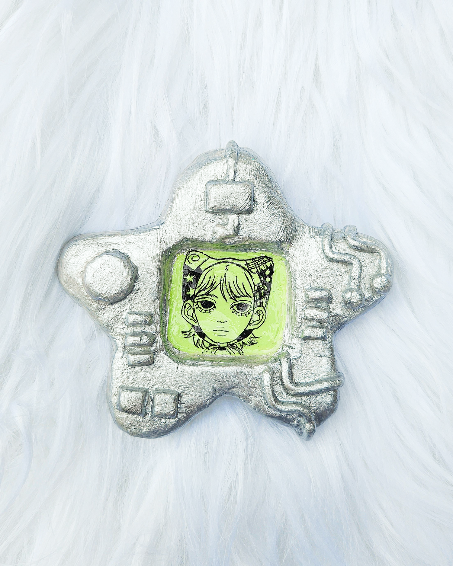 Silver painted clay sculpture in the shape of a star with a sculpted screen. There is a boy drawn with pen in the middle of the screen. The sculpture has circuitboard sci-fi technology-like details. 