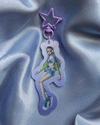 Keychain with lenticular effect of a girl dressed in Y2k Fashion that transitions to a girl dressed in Medieval garb. The clasp is light purple and in a star shape.